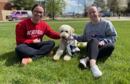 Students sitting on lawn petting a dog